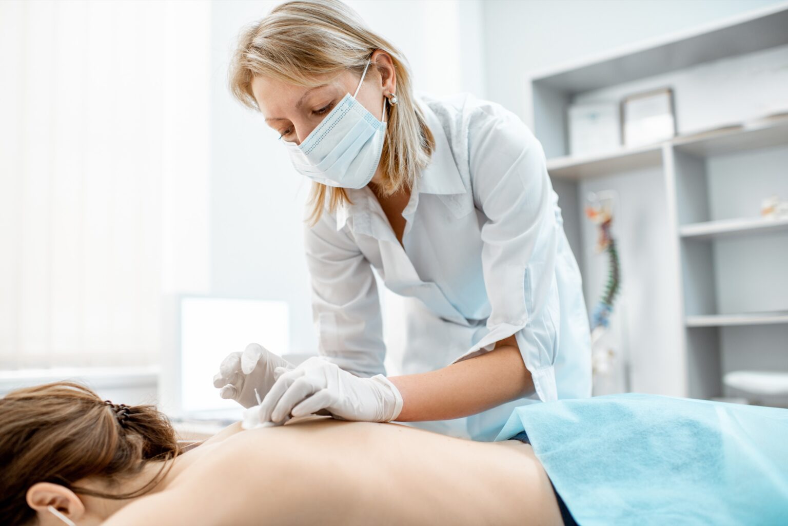 Ärztin mit Mundschutz setzt Akupunkturnadeln am Rücken einer Patientin