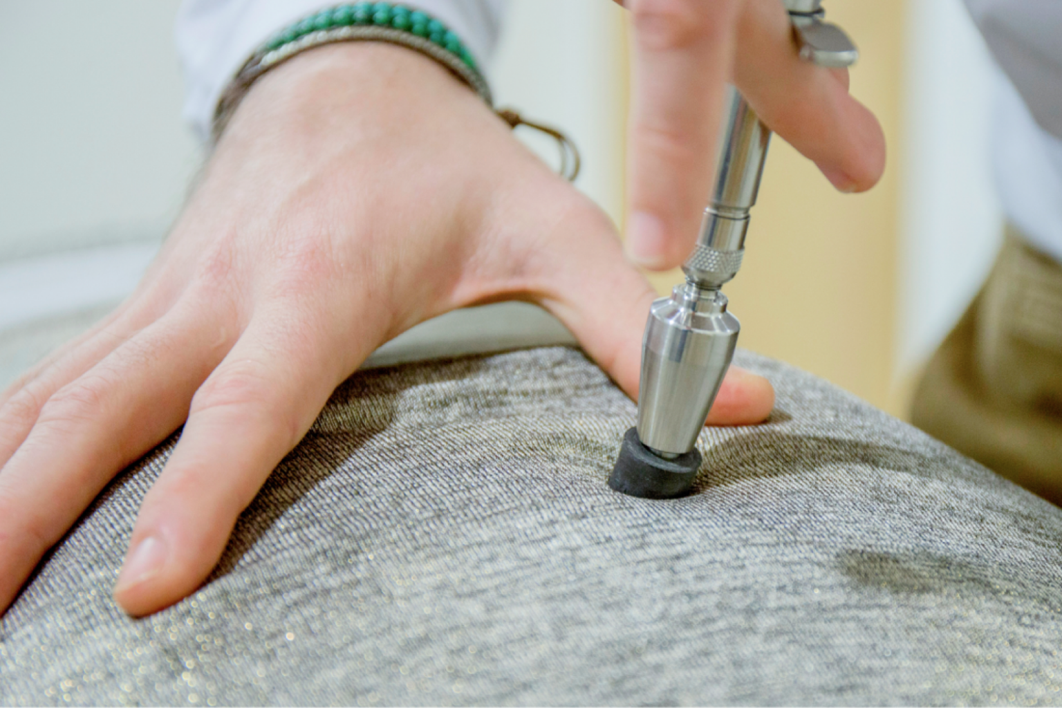 Hand setzt ein metallisches Behandlungsgerät auf grauen Stoff auf