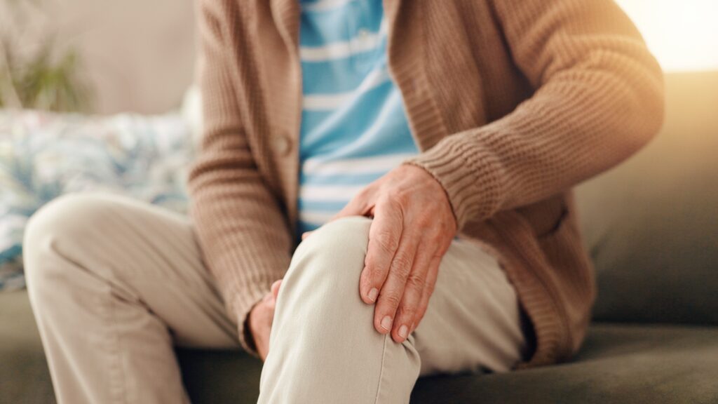 Sitzende Person hält sich das schmerzende Knie