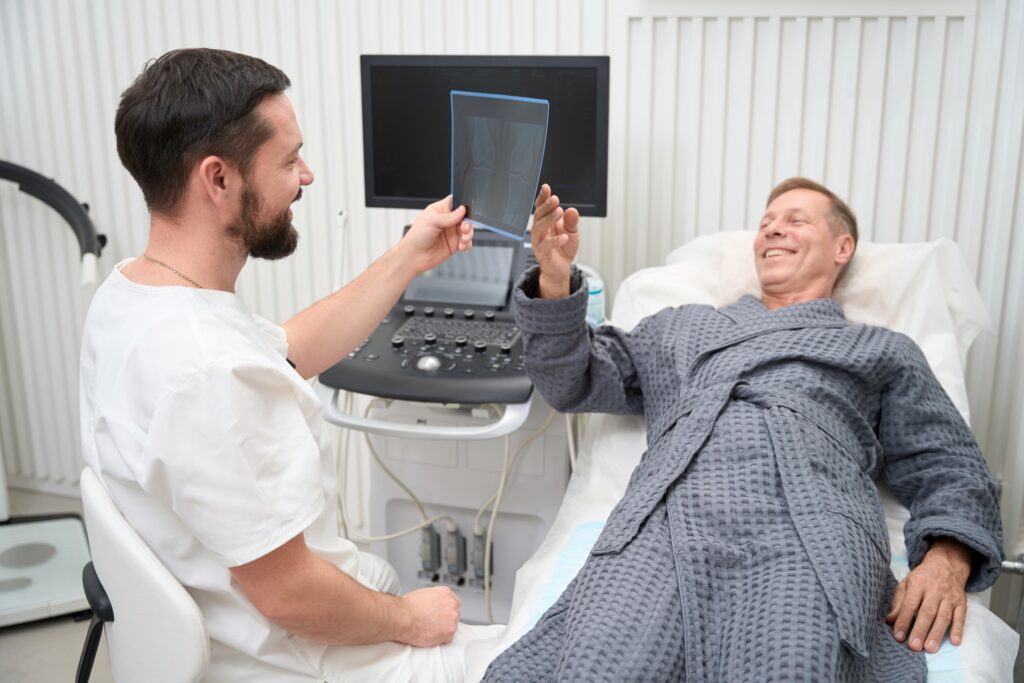 Arzt am Ultraschallgerät neben einem lachenden Patienten im Bademantel