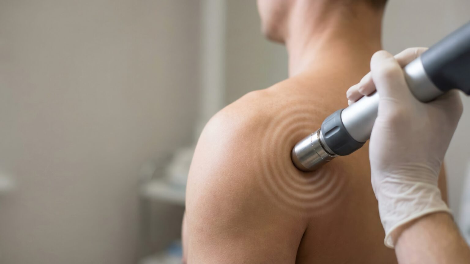 Stoßwellengerät wird an der Schulter eines Patienten angesetzt